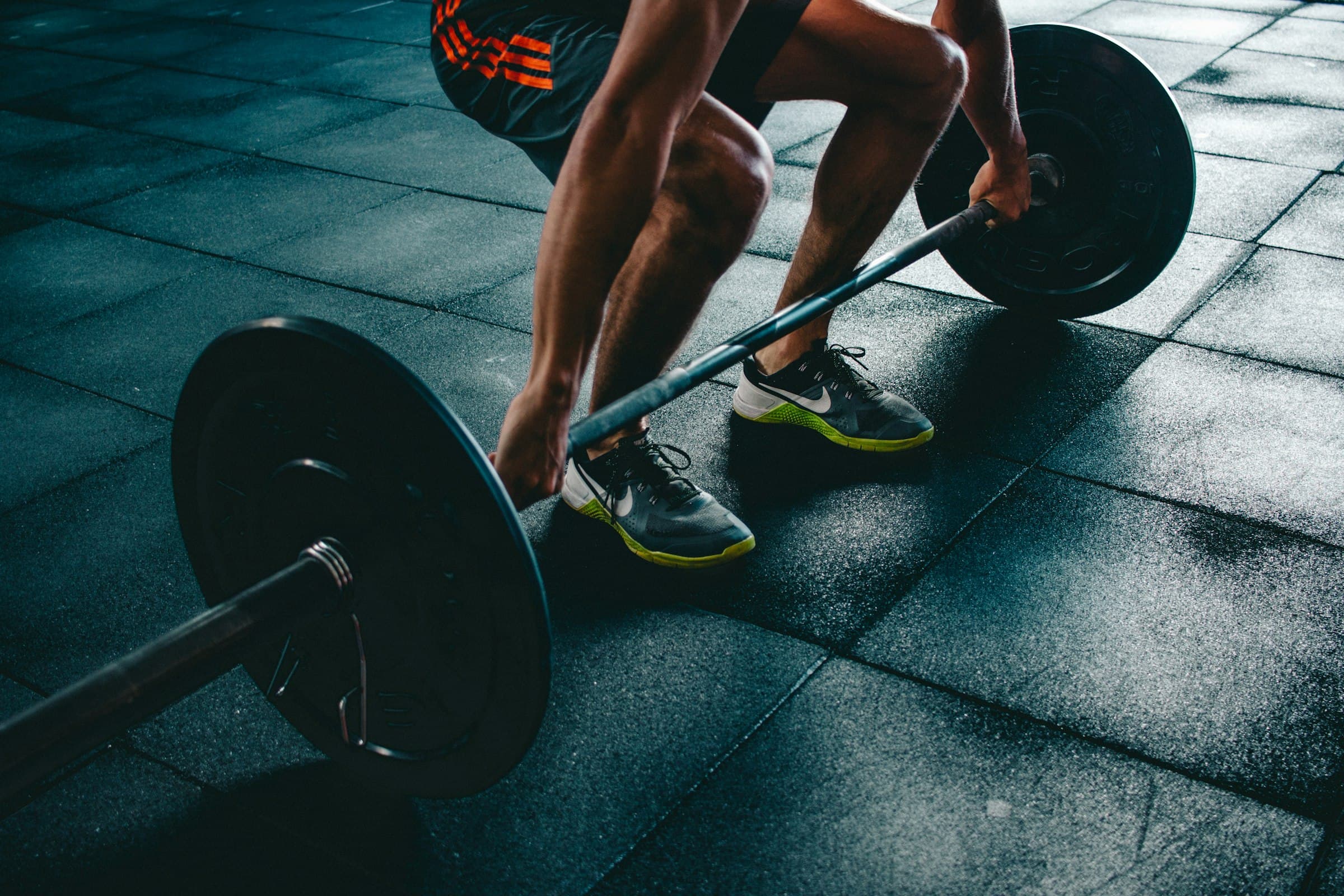 An athlete crouched over a loaded barbell on a gym floor, gripping the bar before a lift