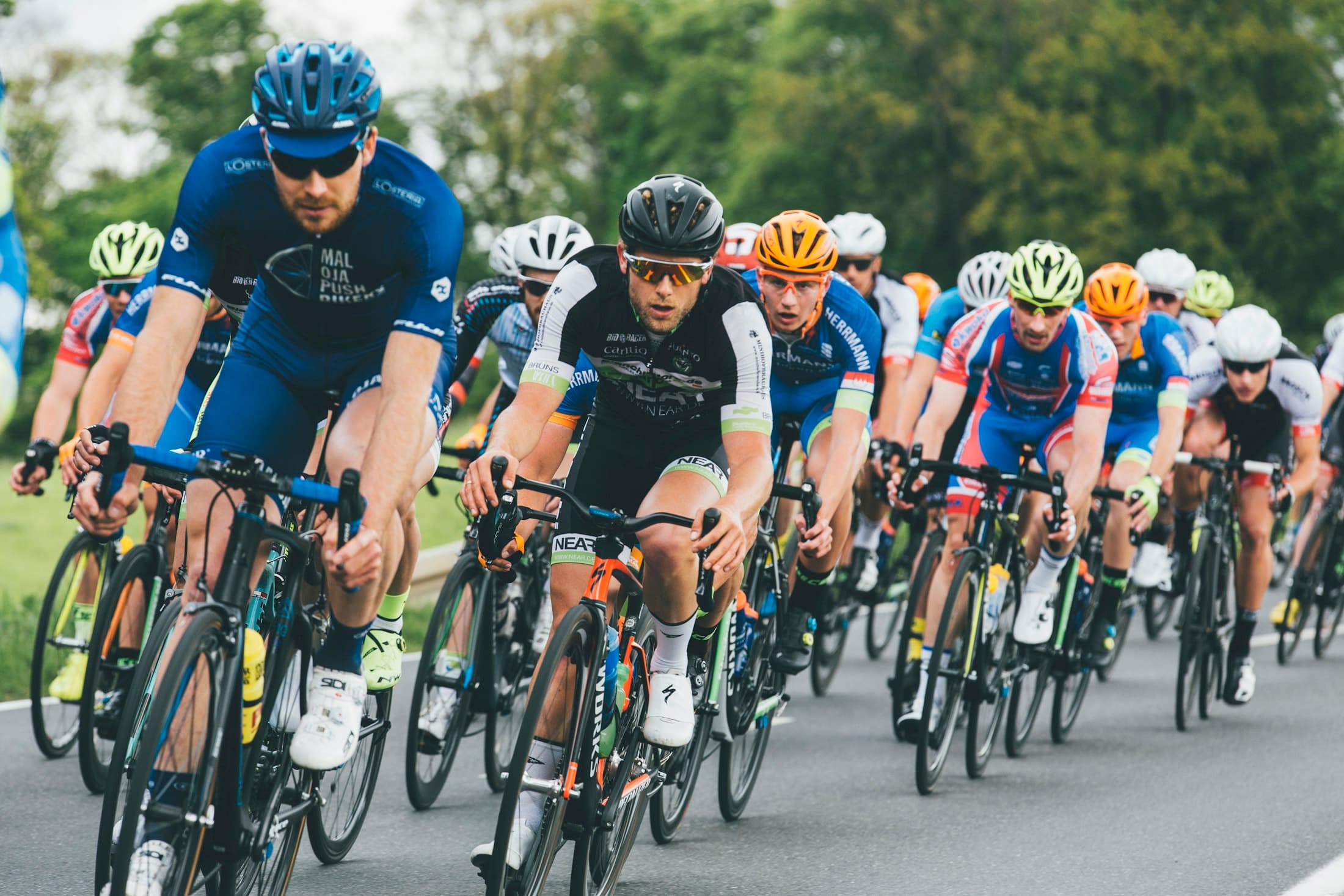 A tight peloton of road cyclists racing along a country road